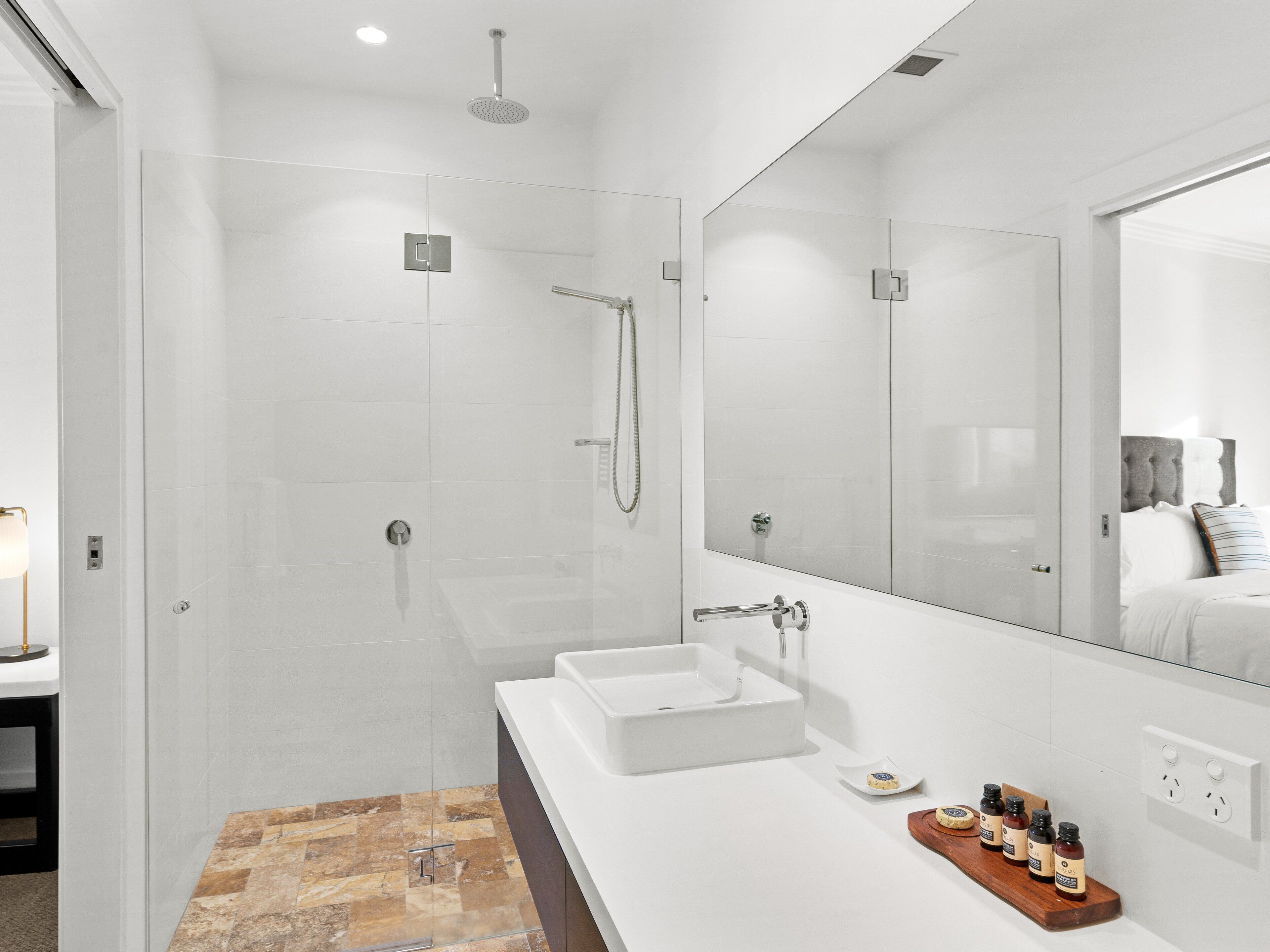 A modern bathroom with a glass-enclosed shower, a white sink, and a large mirror.