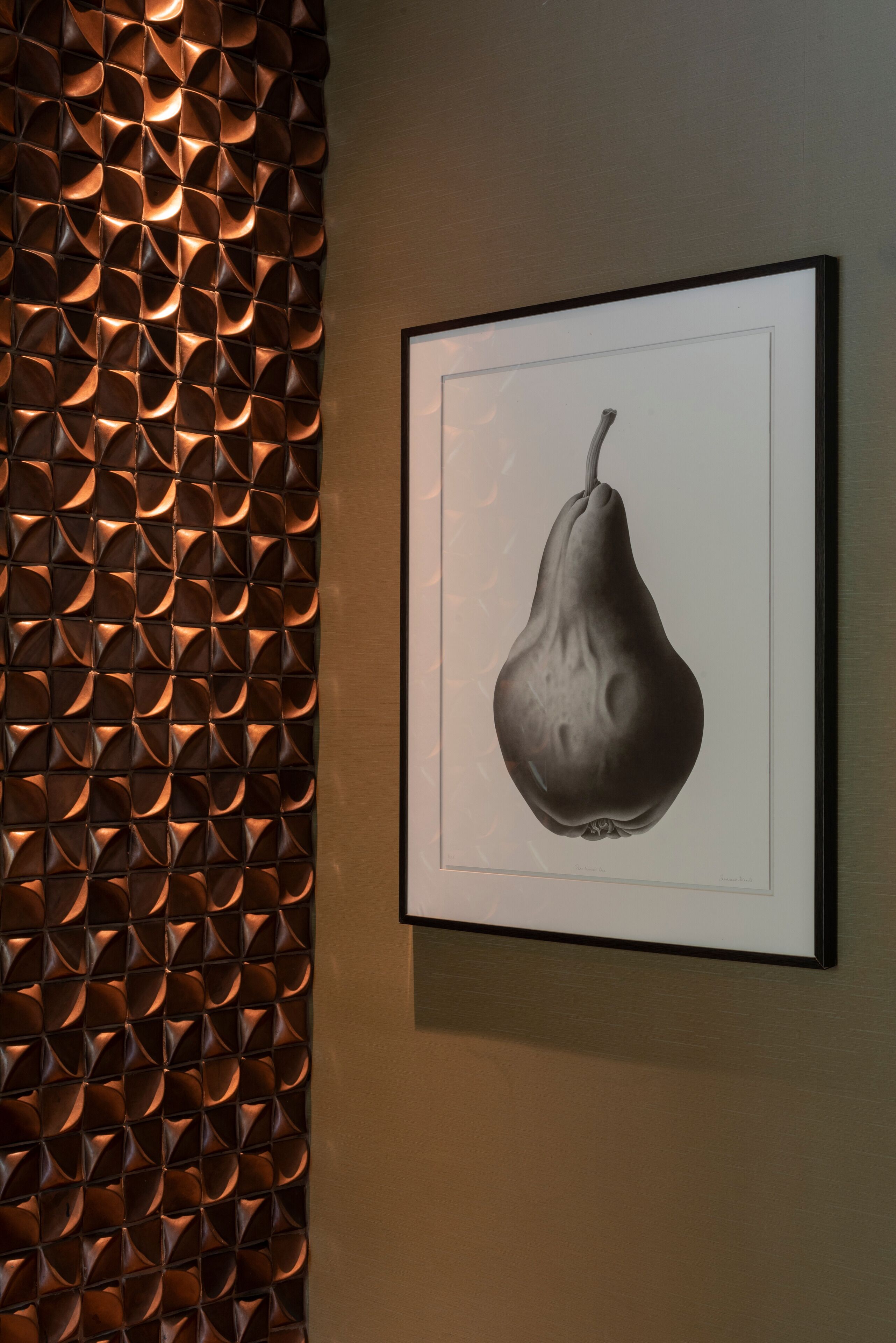 Une photographie en noir et blanc, encadrée, représentant une poire accrochée à un mur.