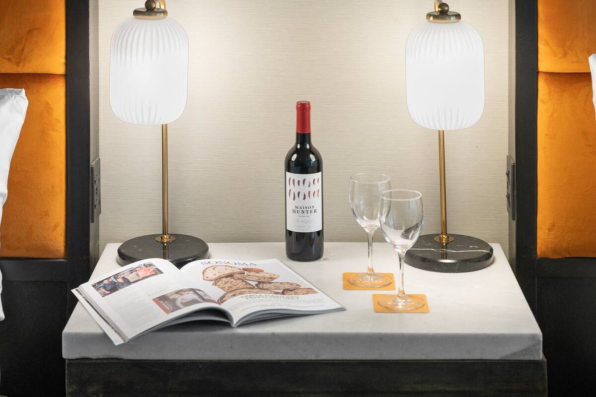 A hotel room with a table set with a bottle of wine, two glasses, and a magazine.