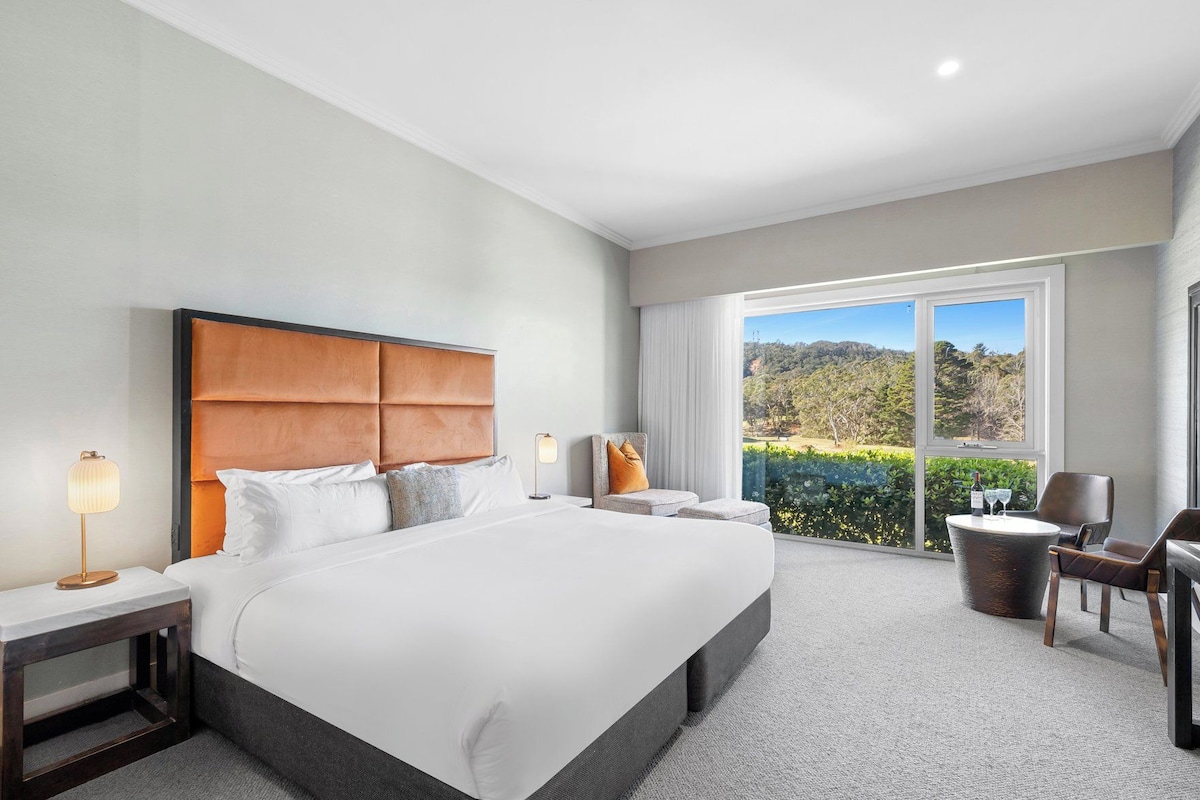 Habitación de hotel con una cama grande, zona de estar con mesa y vistas al exterior.