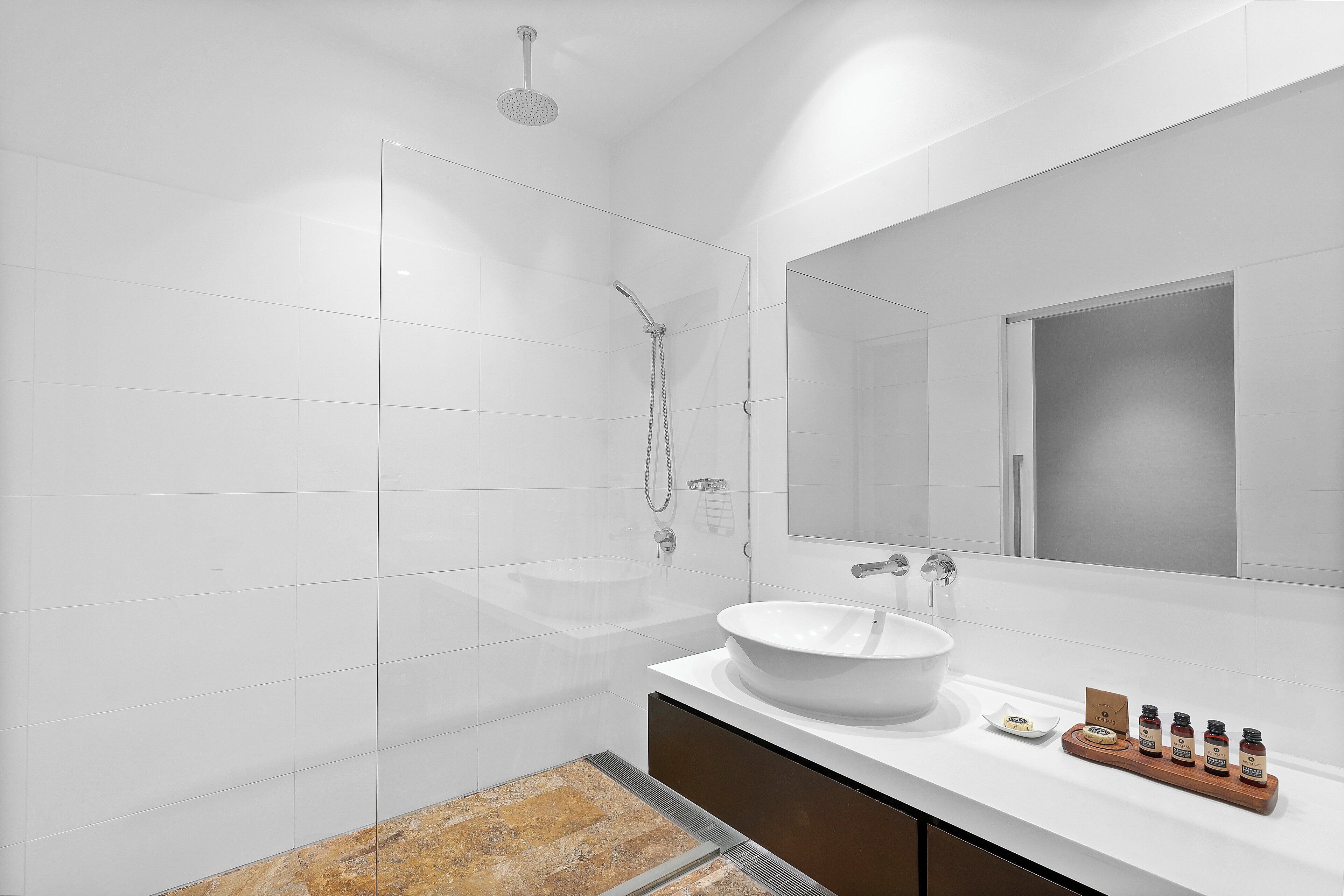 A modern bathroom with a large mirror, a white sink, and a shower area.
