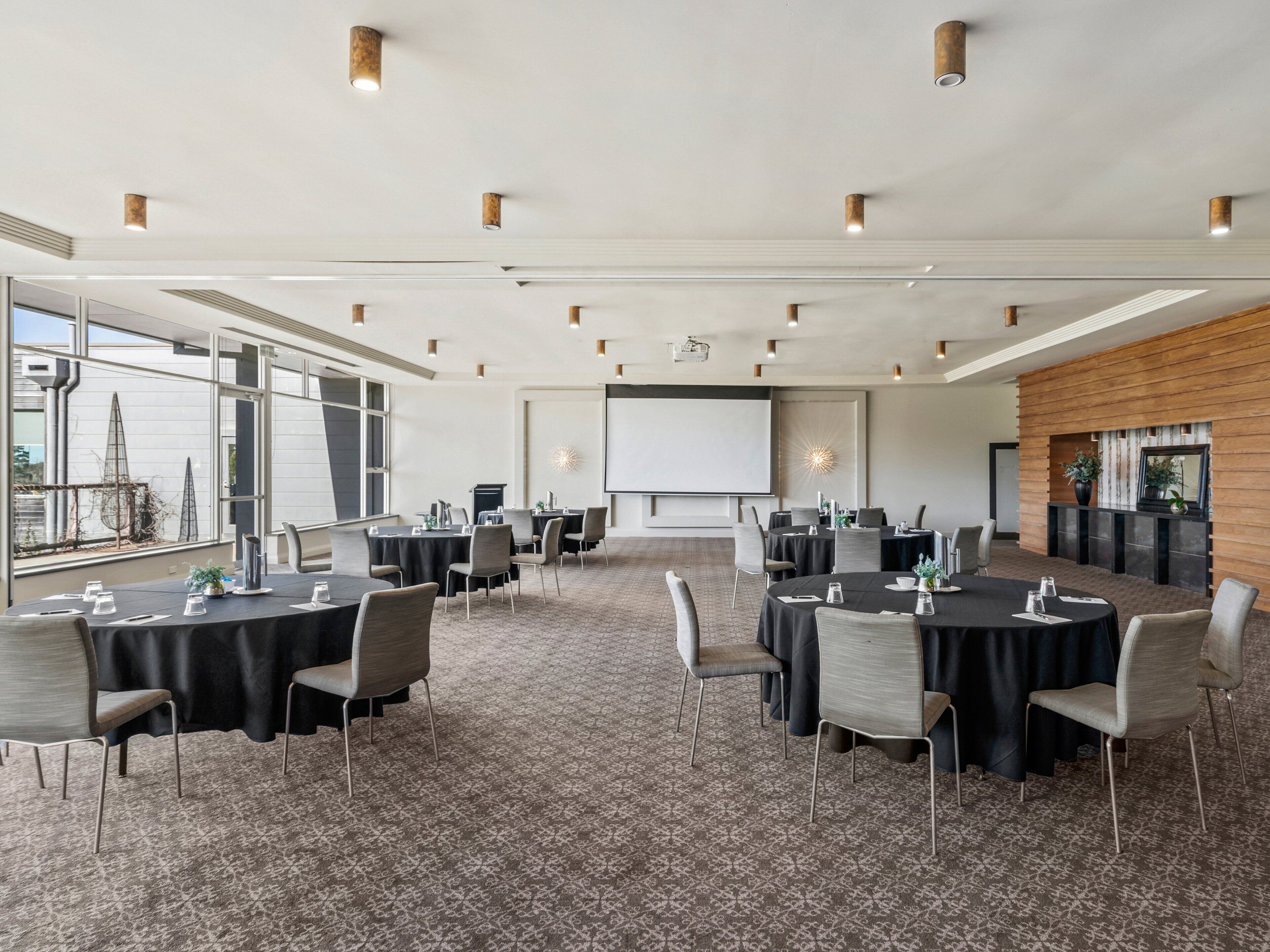 A conference room with multiple tables and chairs, a large screen, and a fireplace.