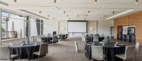 A conference room with multiple tables and chairs, a large screen, and a fireplace.