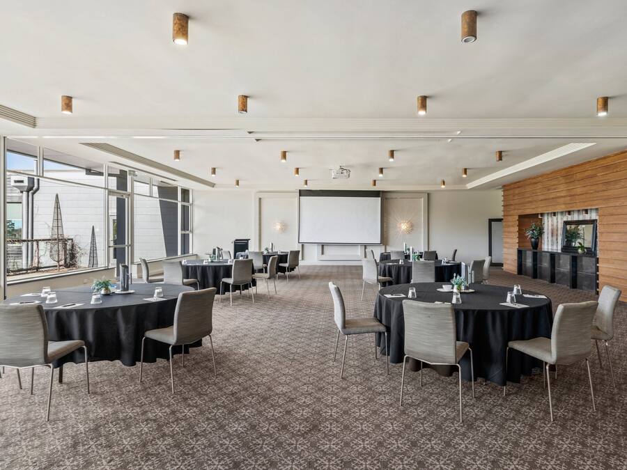 A conference room with multiple tables and chairs, a large screen, and a fireplace.