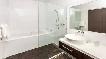 A modern bathroom with a glass-enclosed shower, a freestanding bathtub, a large mirror, and a white sink.