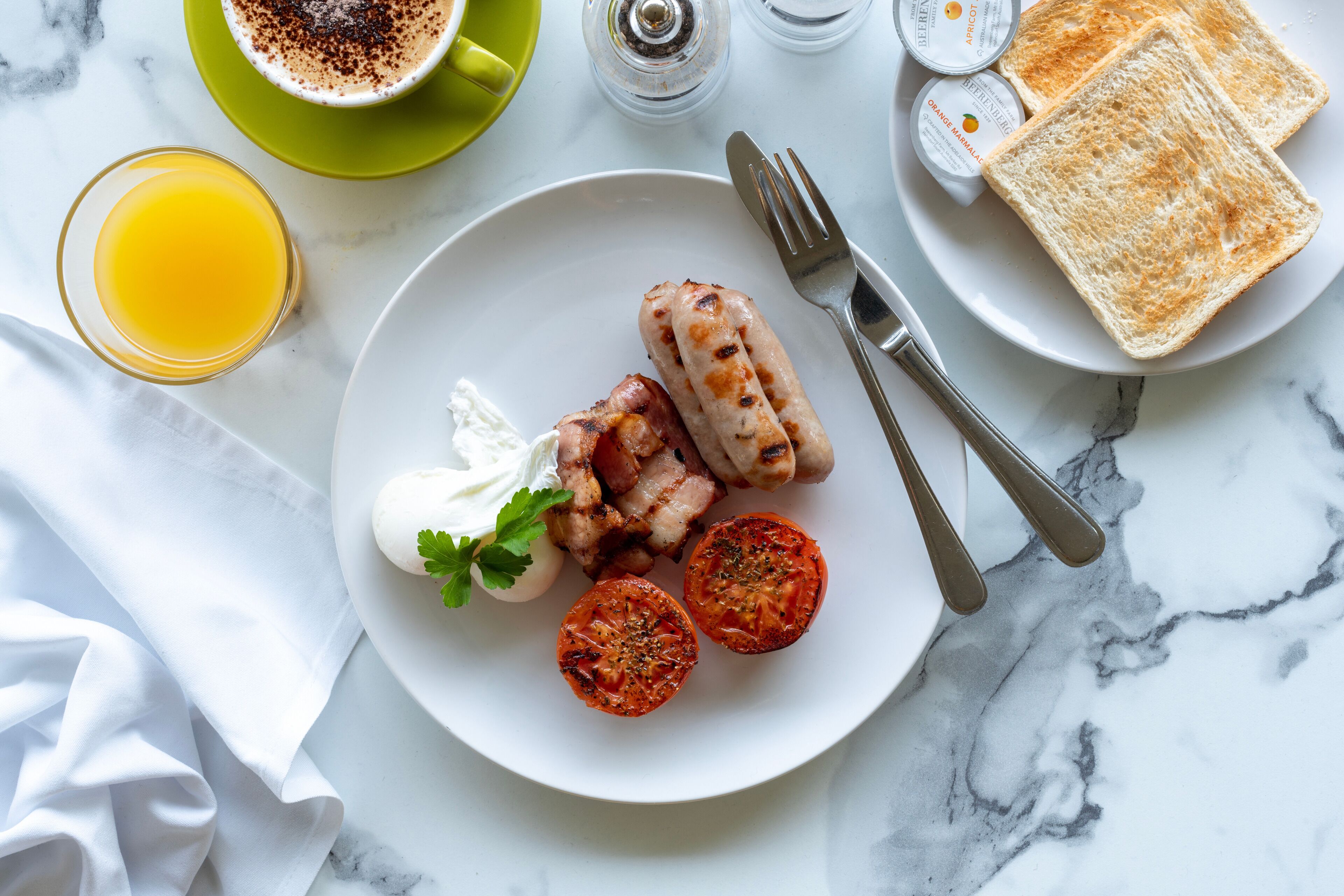 Ein Frühstücksteller mit Würstchen, Tomaten und einem Klecks Sahne auf einem weißen Teller.