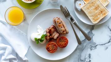 A breakfast plate with sausages, tomatoes, and a dollop of cream on a white plate.