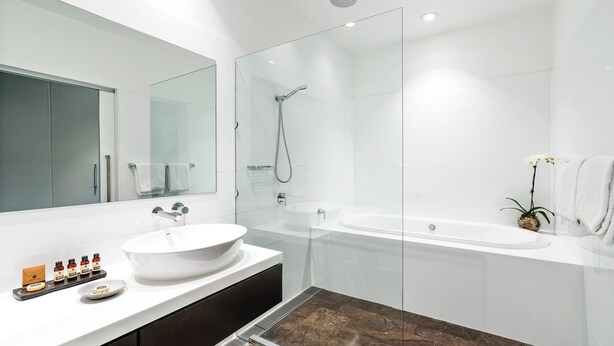 A modern bathroom with a glass-enclosed shower, a large white bathtub, and a vanity with a bowl sink. - The Gibraltar (Bowral)