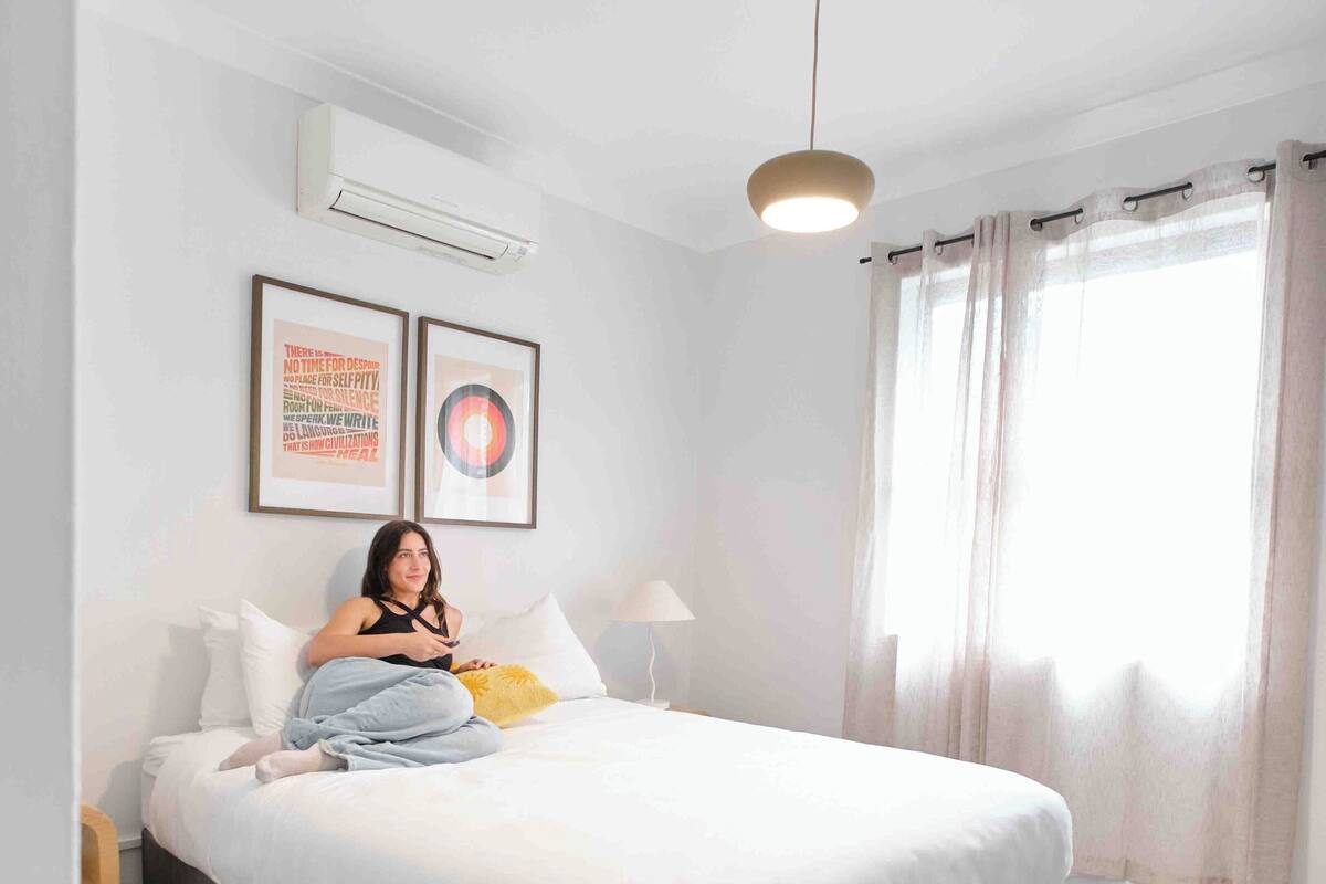Een moderne slaapkamer met een groot bed, een nachtkastje, een lamp en een raam met gordijnen.
