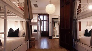 A room with bunk beds, a wooden floor, a patterned rug, and a door leading to another room. - Little Drifter Surry Hills (Redfern)