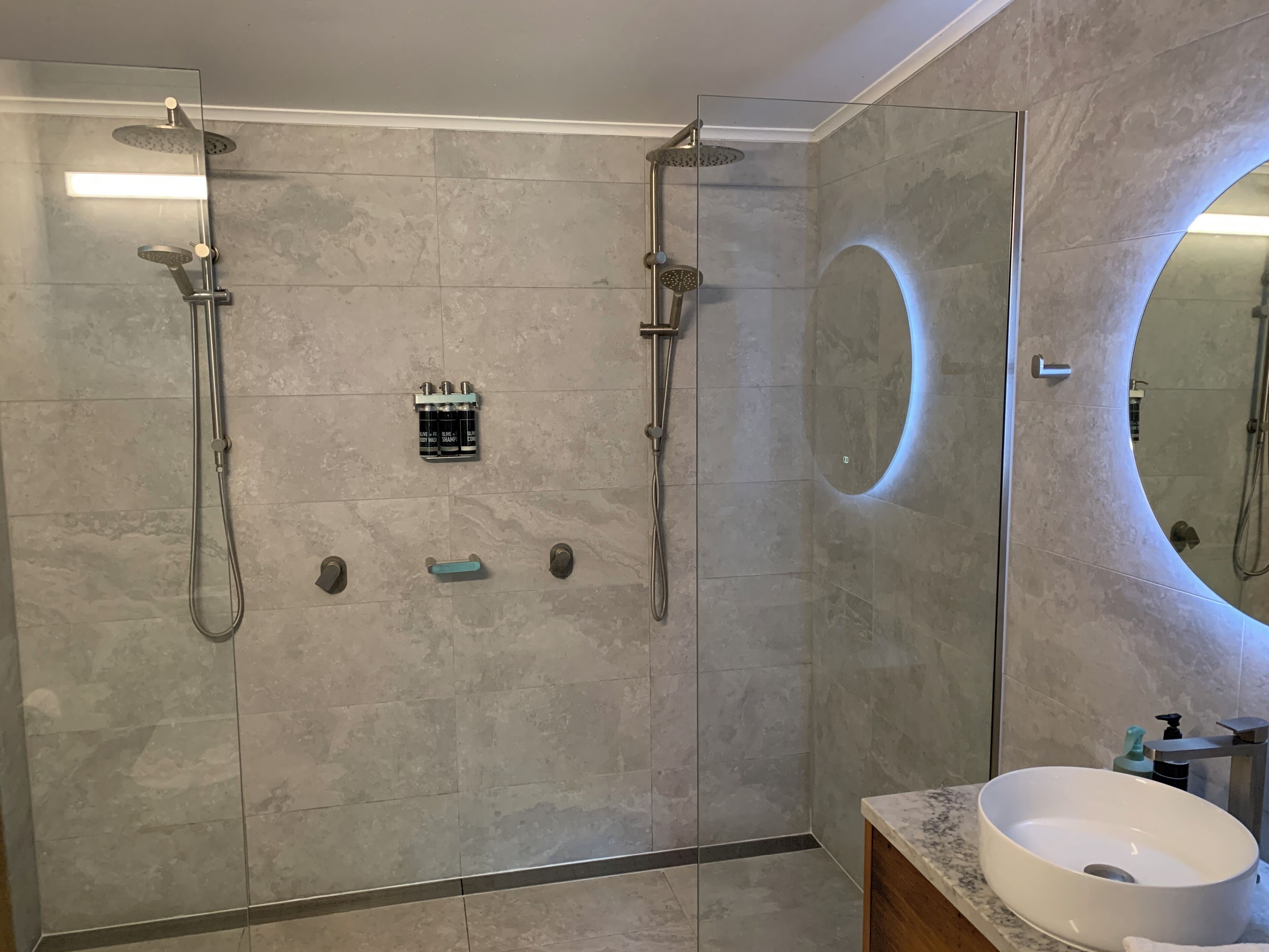 A modern bathroom with a glass-enclosed shower, a large mirror, and a marble sink.