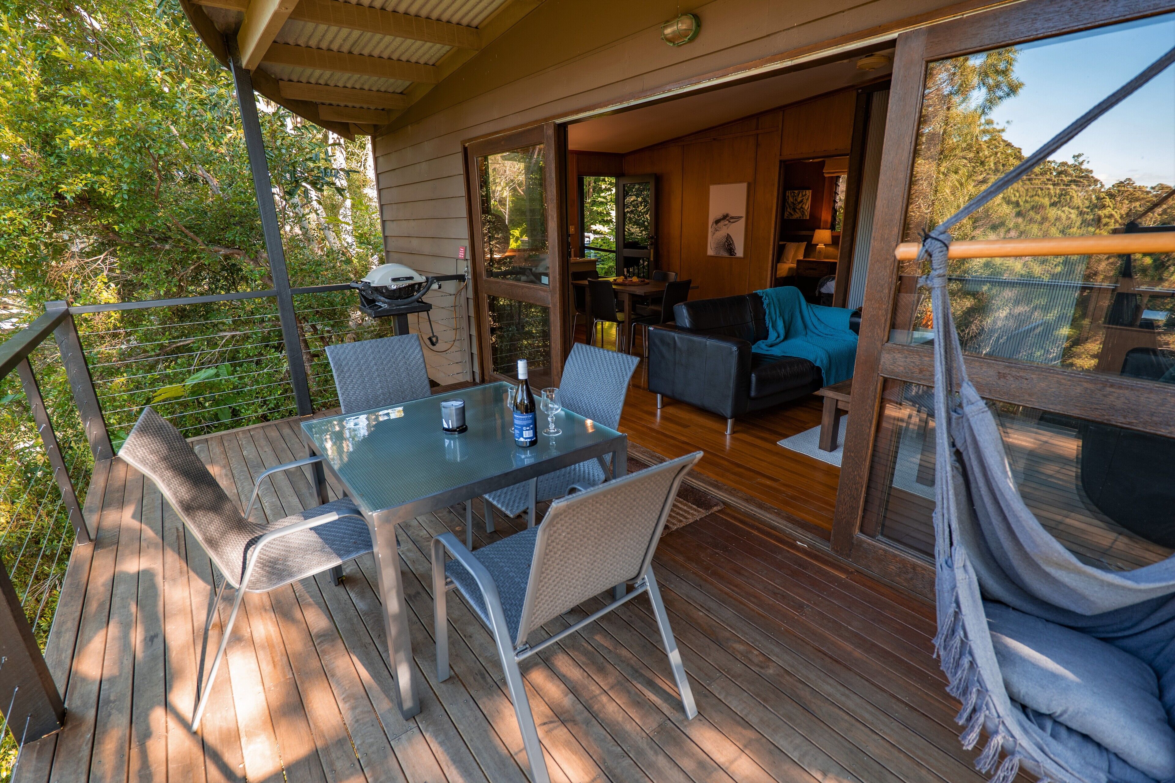 A wooden deck with a glass table and chairs, a hammock, and a view of the interior.