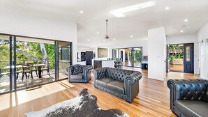 A spacious living area with a large leather sofa, a dining table with chairs, and a glass sliding door leading to a balcony. - Whispering Valley Cottage Retreat (Witta)