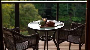 A round table with two wicker chairs on a wooden deck, a candle, a mug, and a plate with food.