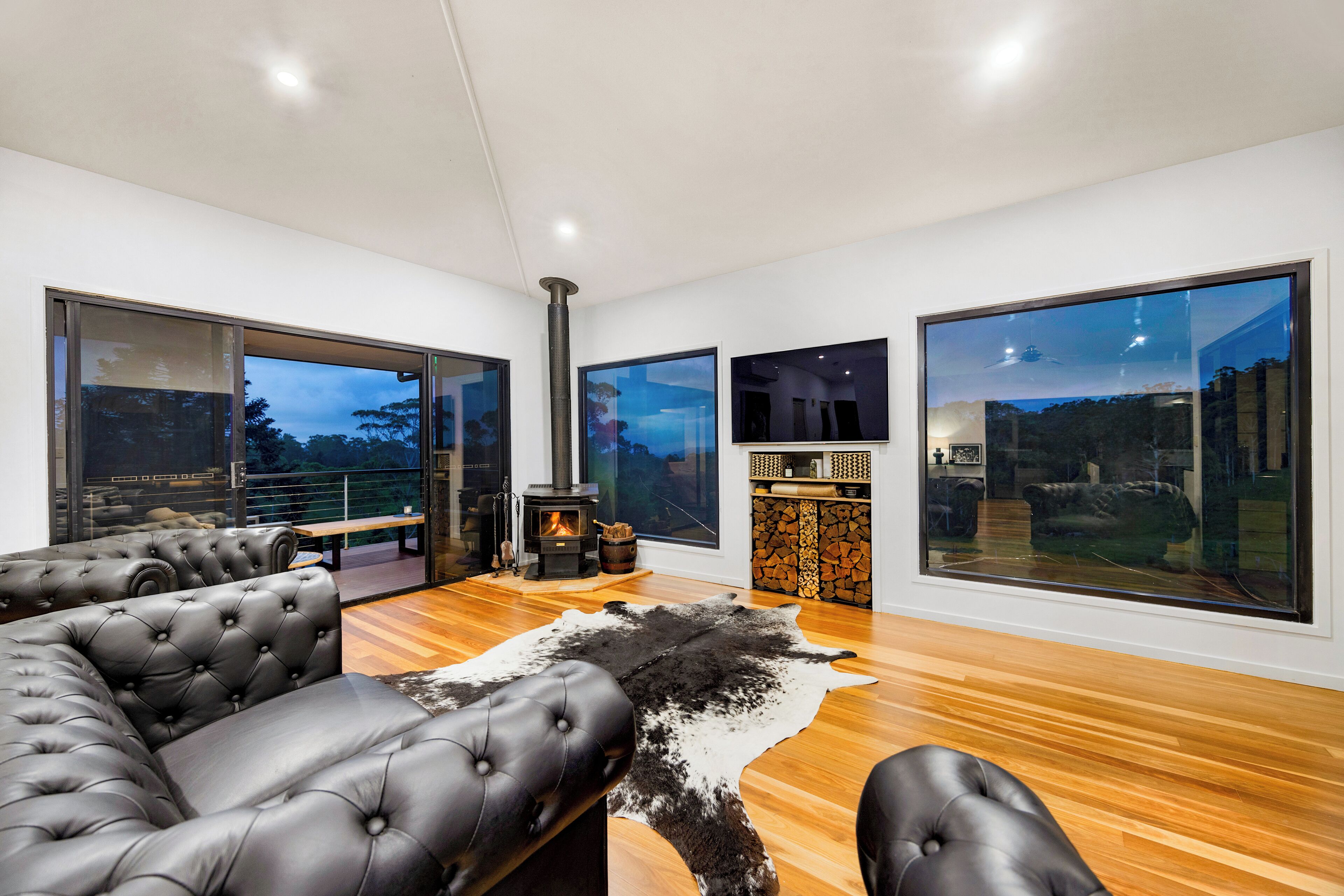 A modern living room with a fireplace, leather sofas, a large window, and a stone fireplace surround.