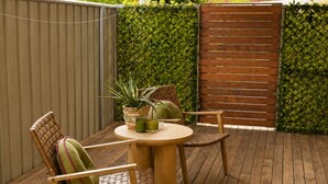 An outdoor patio with a wooden table and chairs, a covered area, and a green hedge wall. - Muswellbrook Motor Inn (Muswellbrook)