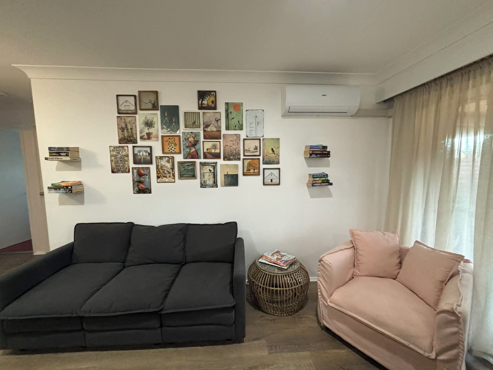 A living room with a black sofa, a pink sofa, and a wall decorated with various framed pictures and books.