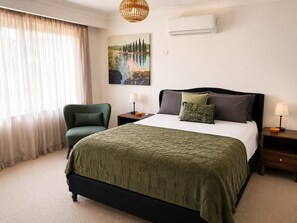 A hotel room with a bed, a chair, a painting, an air conditioner, and a lamp. - Muswellbrook Motor Inn (Muswellbrook)