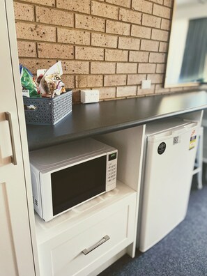A kitchenette with a microwave, a small refrigerator, and a basket of groceries on the counter.