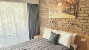 A hotel room with a bed, a nightstand, a wall-mounted painting, and a window with curtains. - Muswellbrook Motor Inn (Muswellbrook)