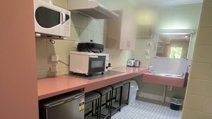 A compact kitchen with a microwave, toaster, and small refrigerator. There are bar stools and a sink with a mirror above it.