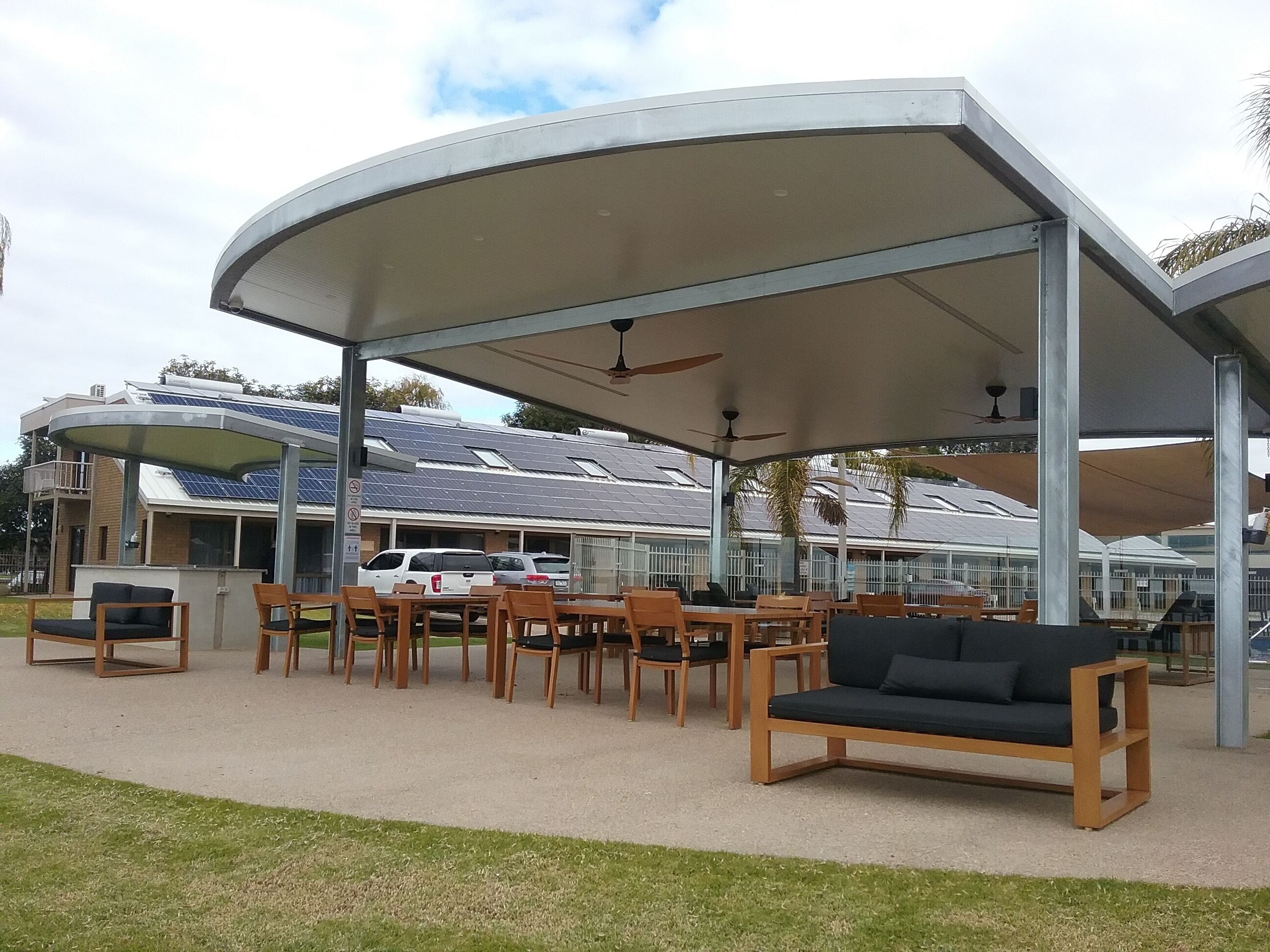 An outdoor seating area with tables and chairs, a covered pavilion, and a building with solar panels in the background.