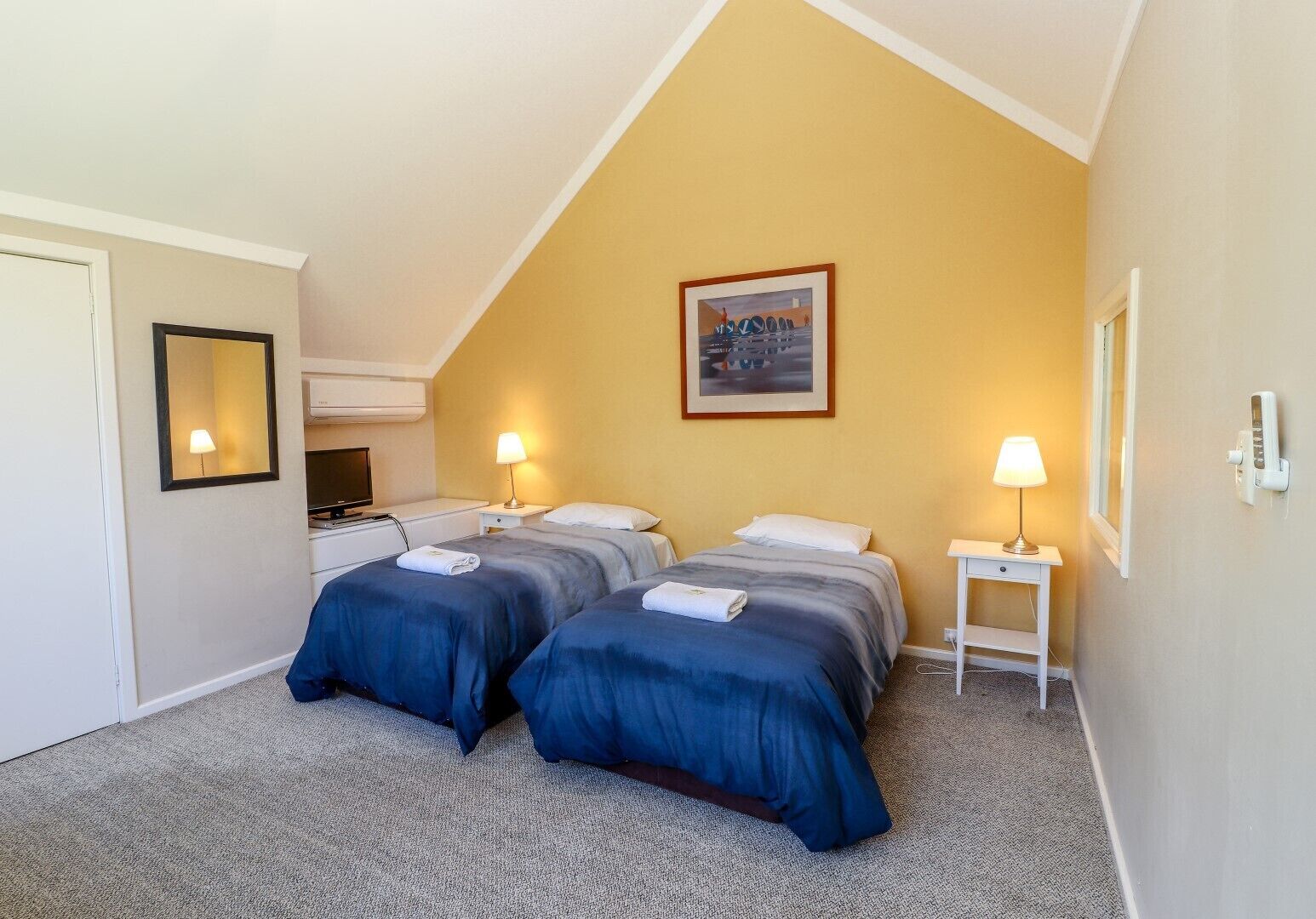 Habitación de hotel con dos camas, un cuadro en la pared, un escritorio con lámpara y un teléfono también en la pared.