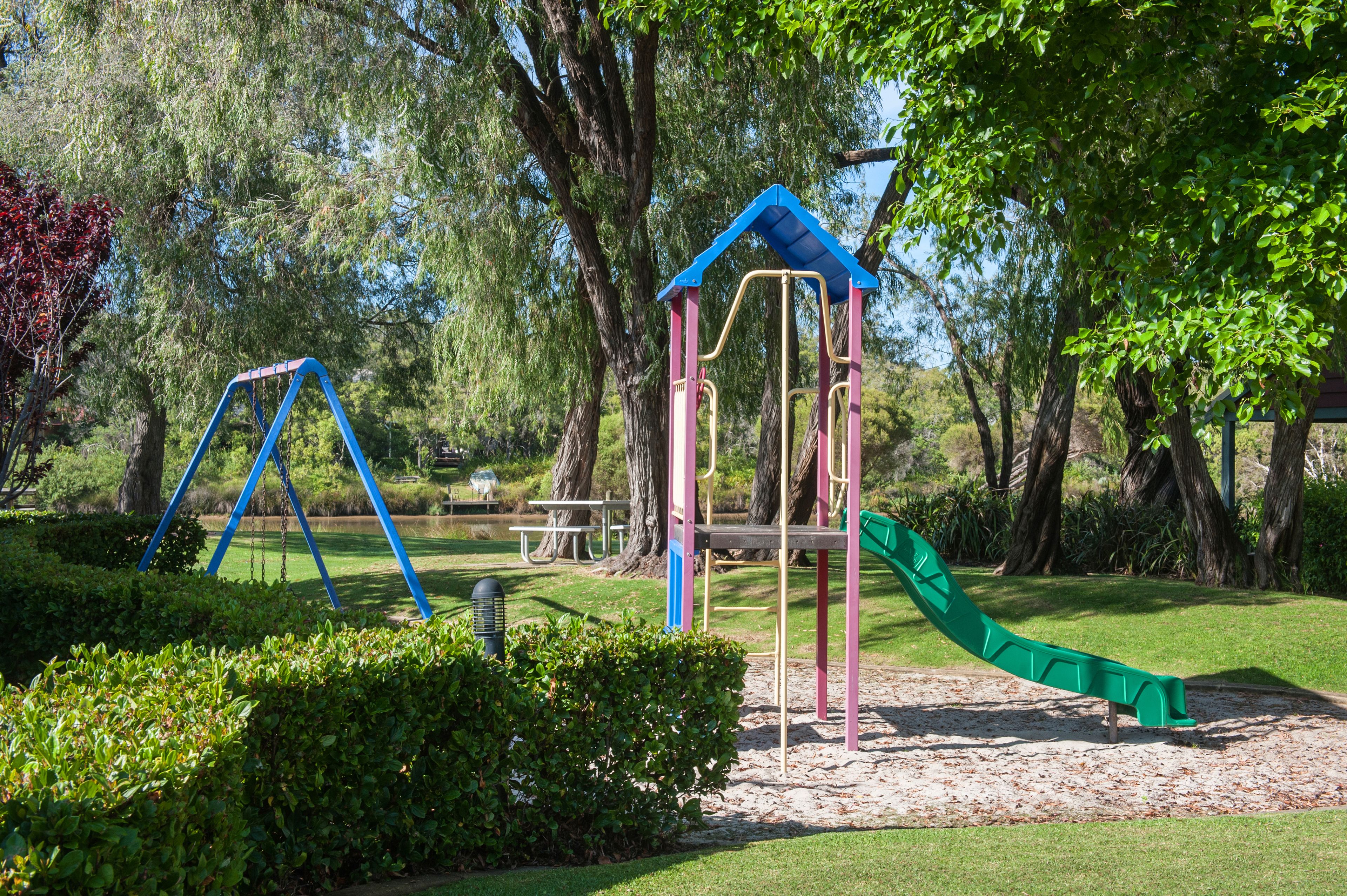 A playground with swings, a slide, and picnic tables in a park with trees.