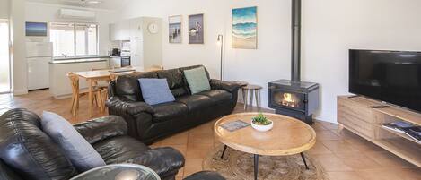 A modern living room with a black leather sofa, a wooden coffee table with a plant, a TV, and a wood-burning stove.