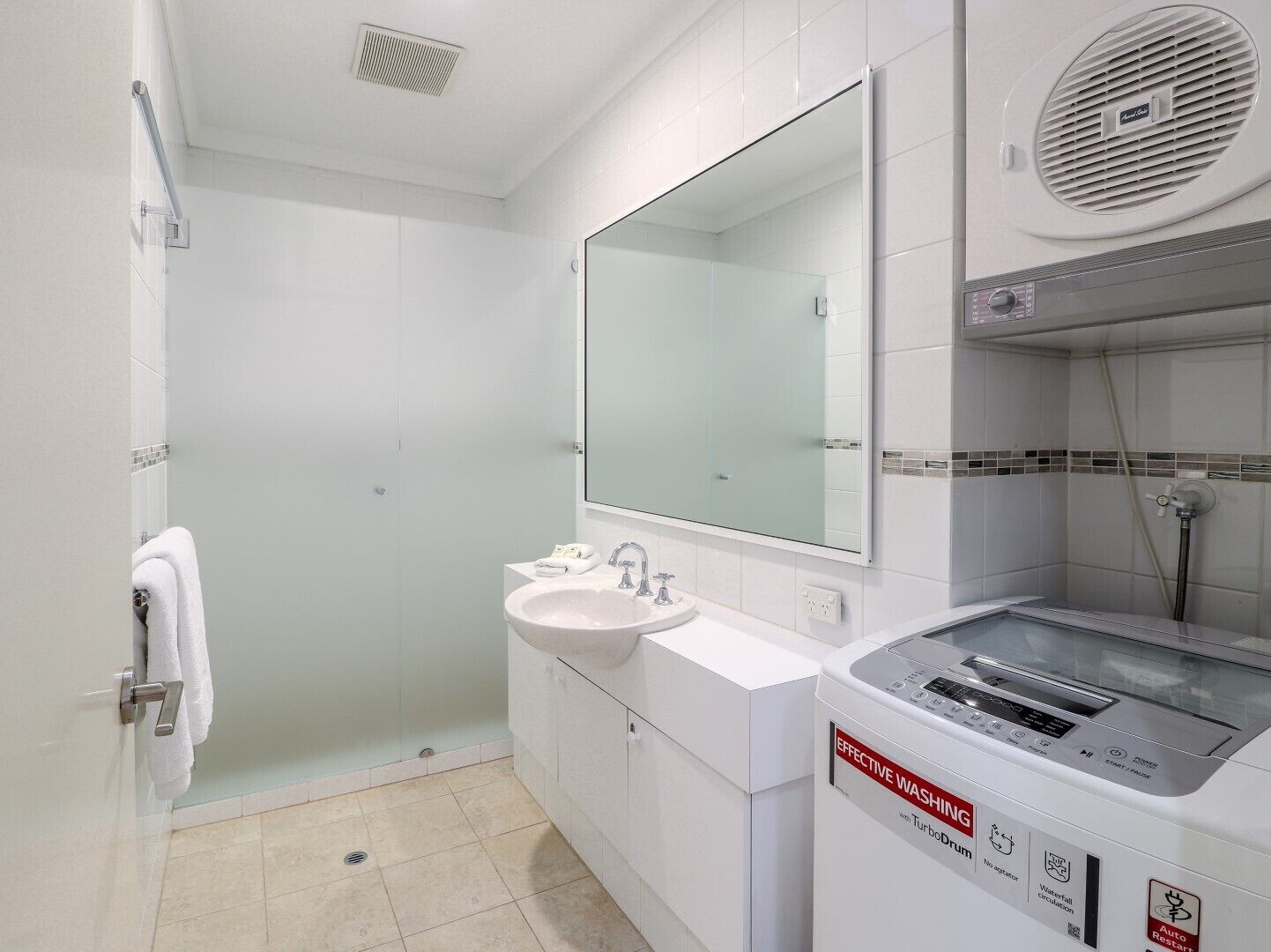 A modern bathroom with a glass shower enclosure, a sink with a mirror, and a built-in washing machine.