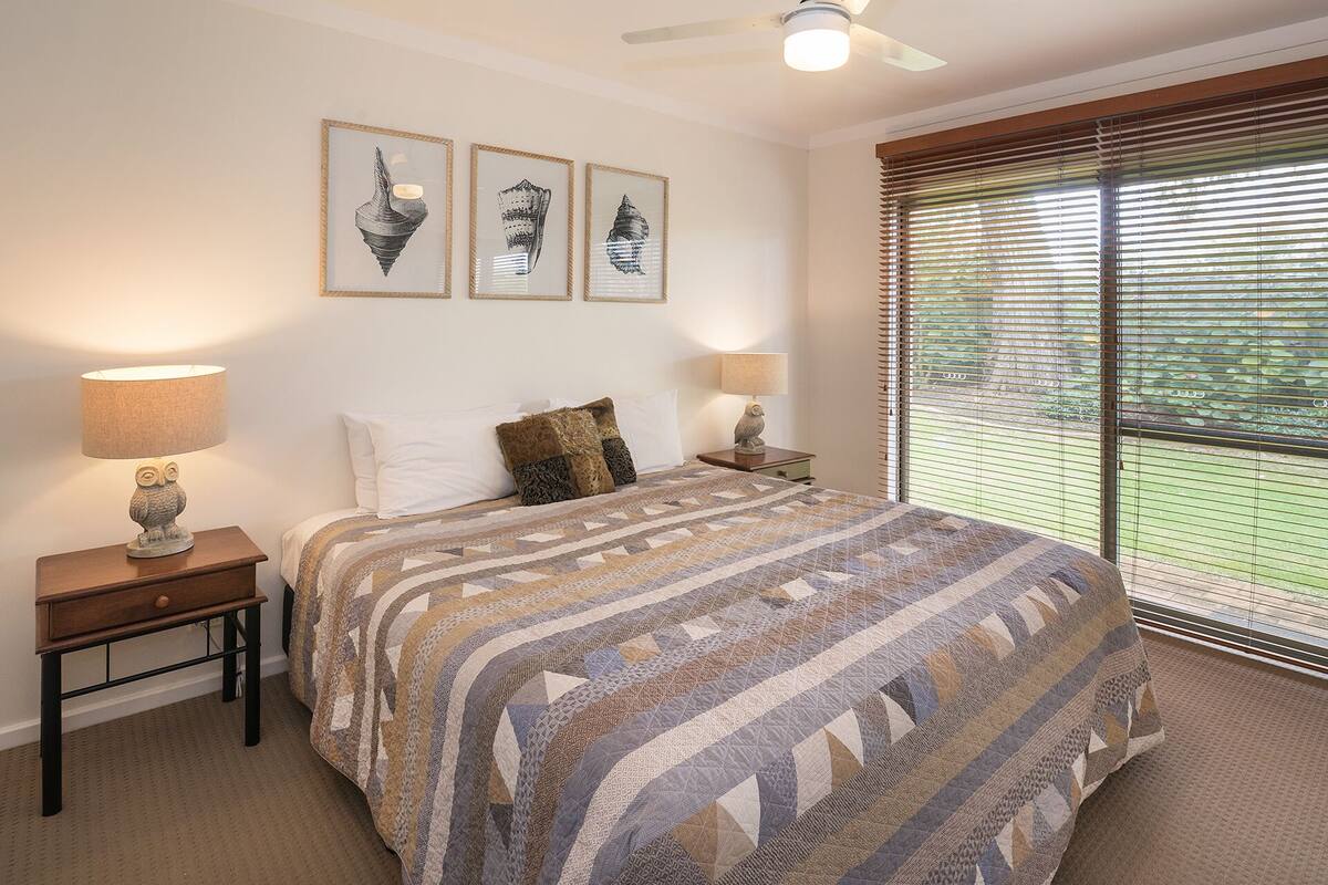 A bedroom with a large bed, two bedside lamps, and three framed pictures on the wall.