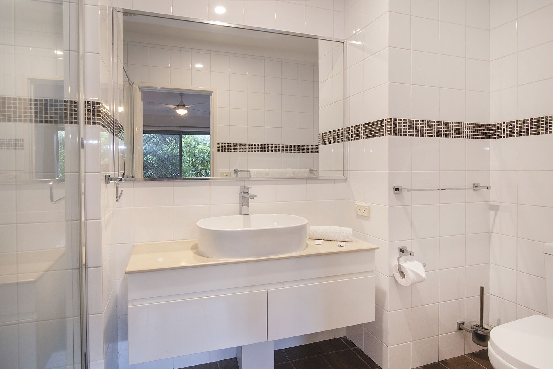 Ein modernes Badezimmer mit einem großen Spiegel, einem weißen Waschbecken, einer Toilette und einer Duschkabine.