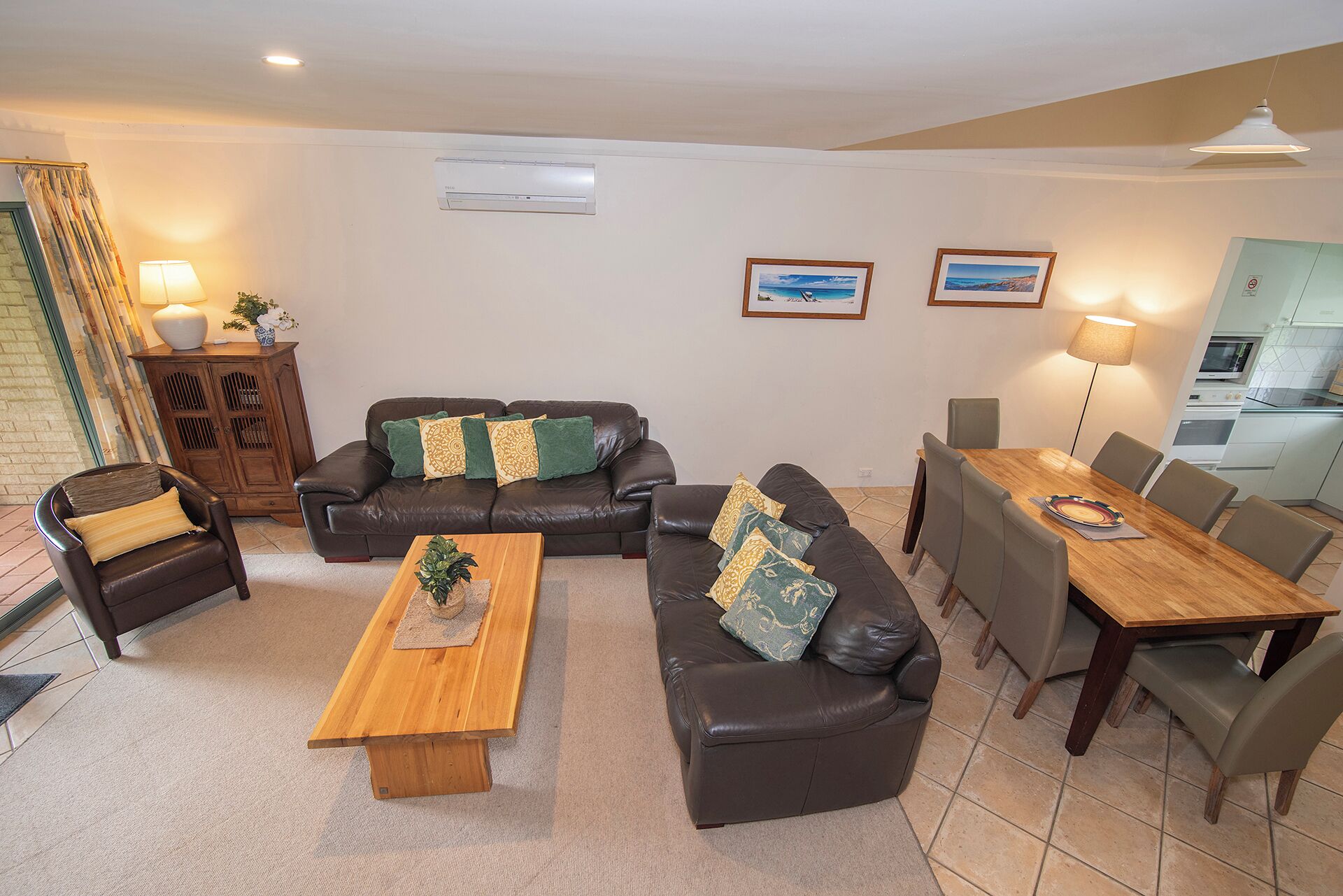 En stue med sofaarrangement, et træbord, et spisebord med stole og et køkken i baggrunden.