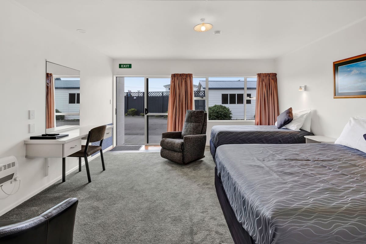 Une chambre d’hôtel équipée d’un bureau, de deux lits, d’une chaise et offrant une vue sur l’extérieur.