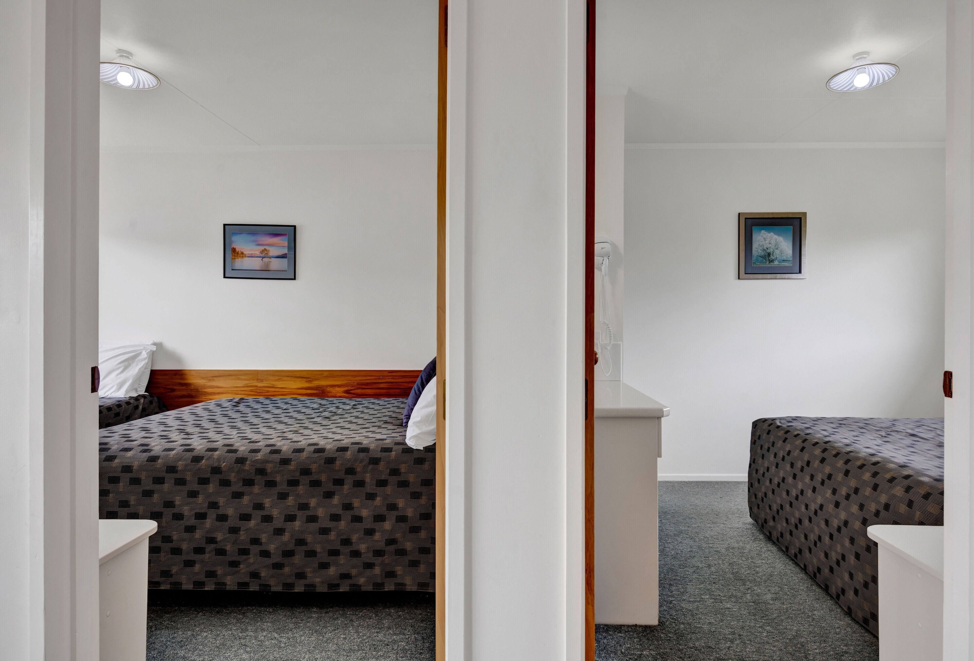 A room with two beds, a small white desk, and two framed pictures on the walls.