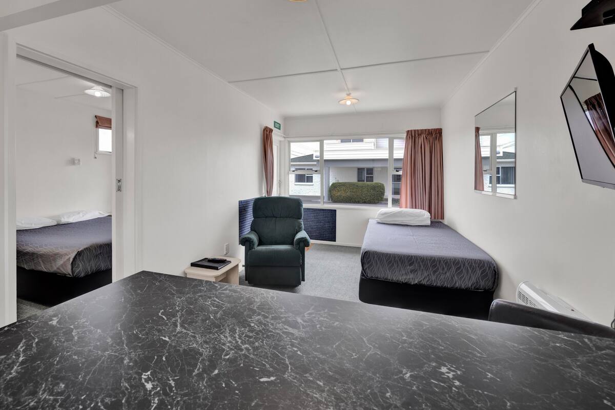 Une chambre d’hôtel moderne avec une table en marbre, deux lits simples, une chaise et une fenêtre avec des rideaux.