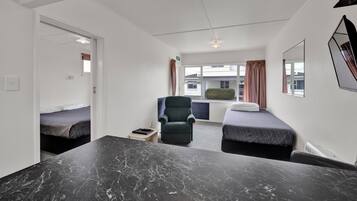A modern hotel room with a marble table, two single beds, a chair, and a window with curtains.