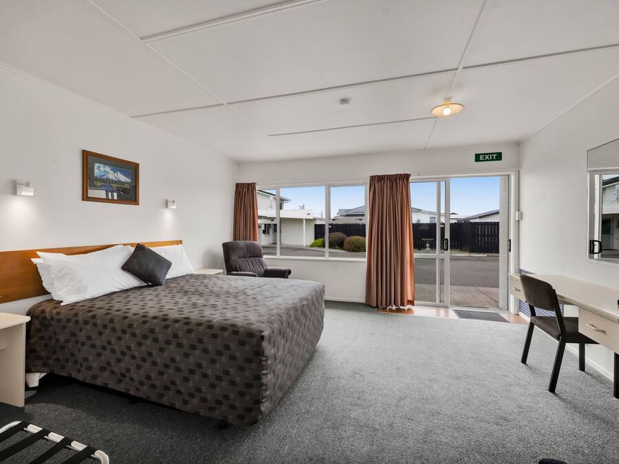 A hotel room with a bed, a desk, a chair, and a view of the outside.