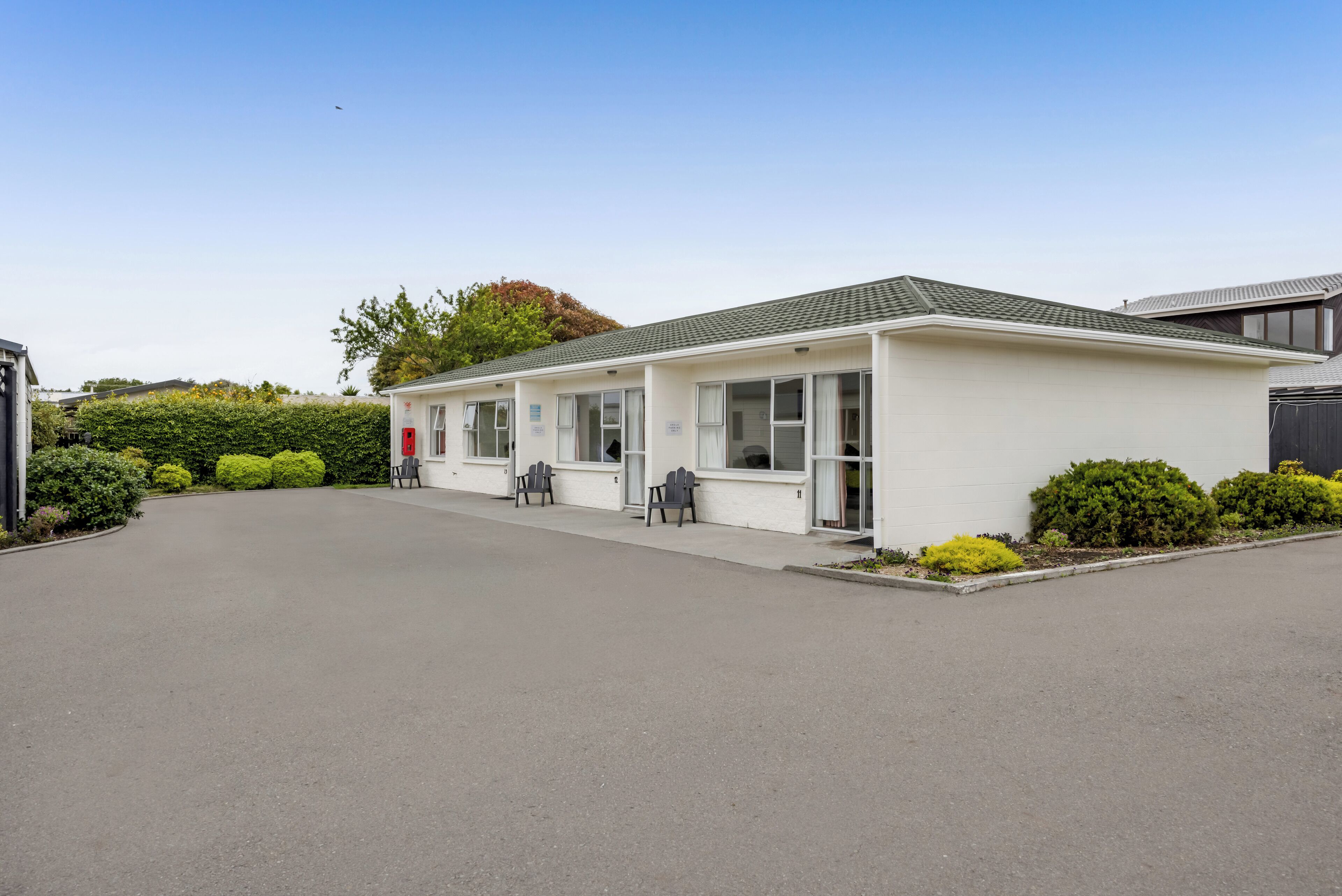 A single-story motel with a parking lot, a covered outdoor seating area, and a small garden.