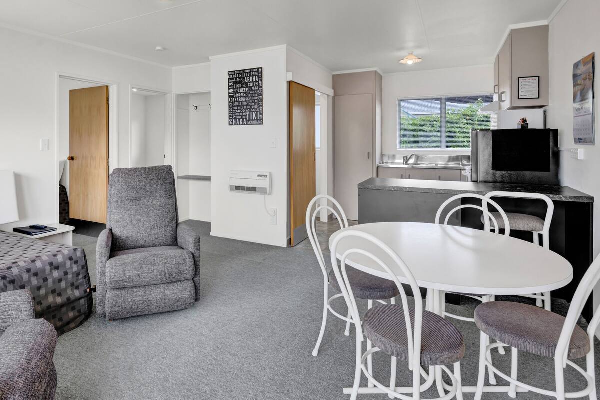 Une pièce moderne et bien éclairée, comprenant un canapé, un fauteuil et une table à manger. On y trouve également un coin cuisine avec un réfrigérateur et une fenêtre.