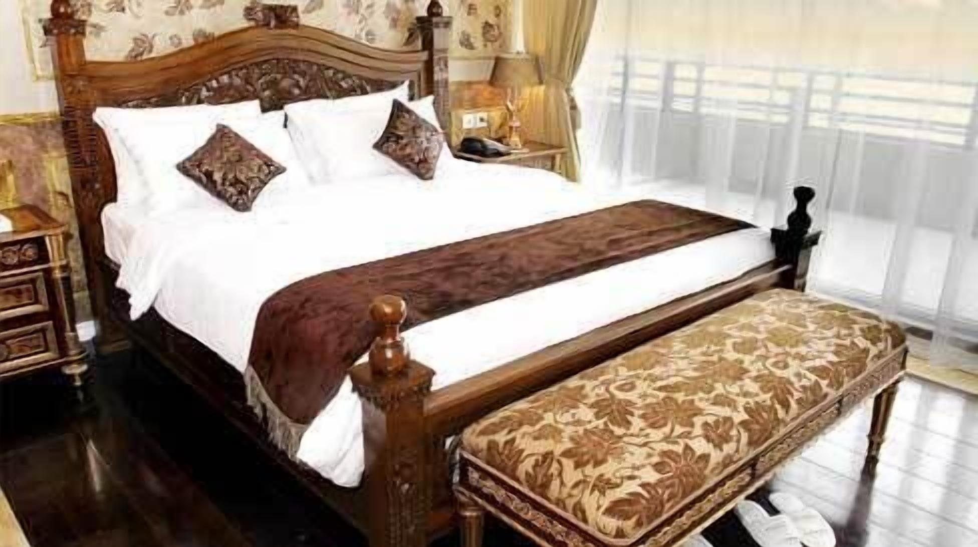 A large bed with a wooden headboard, white bedding, and a bench at the foot of the bed.