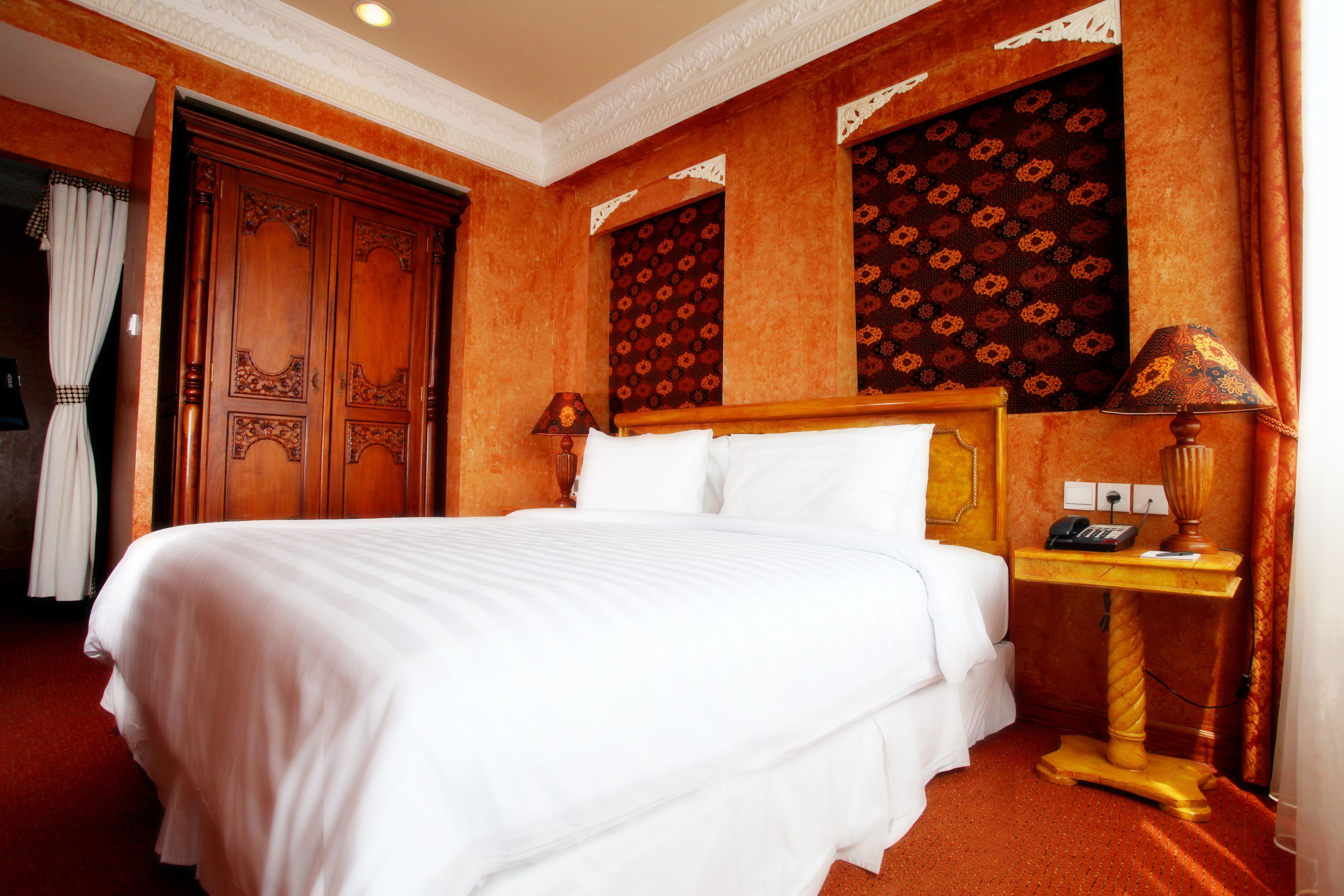 A hotel room with a large bed, wooden wardrobe, and a small bedside table with a lamp.