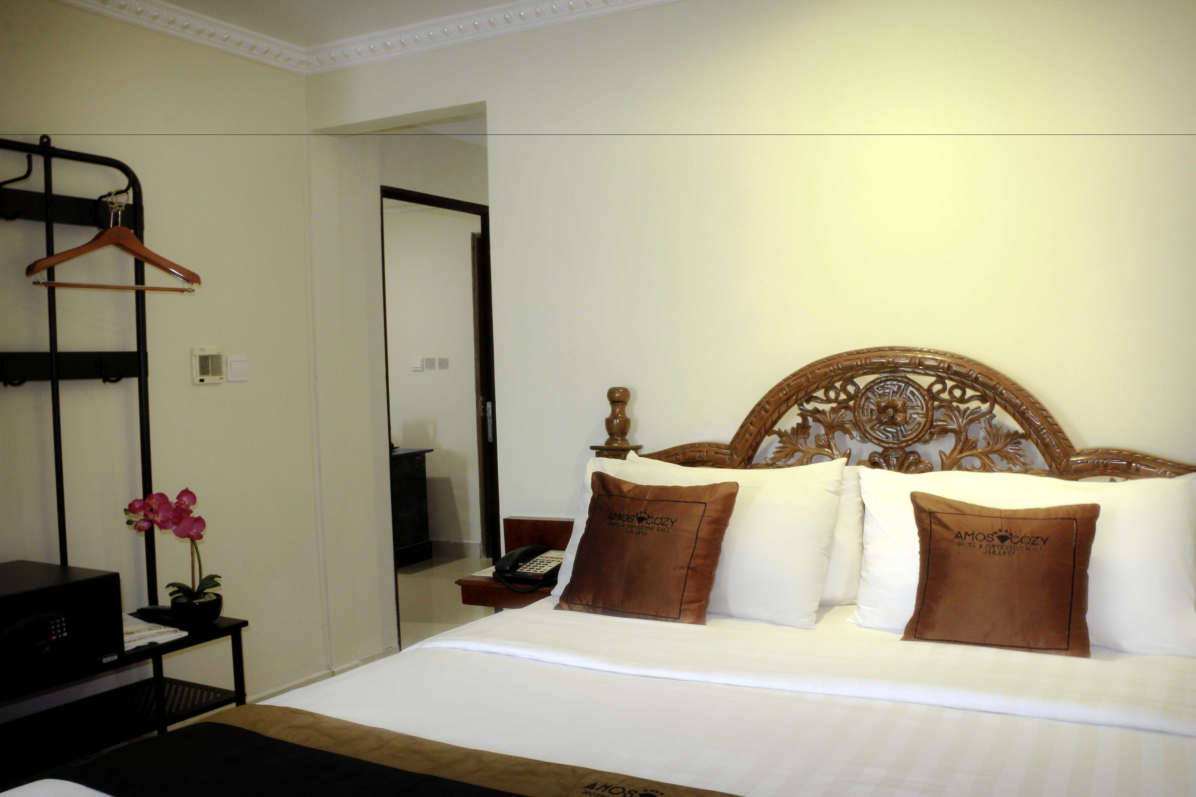 A neatly made bed with a wooden headboard, a bedside table with a phone, and a hanging coat rack.
