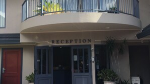 Un área de recepción con un balcón, una puerta roja y plantas en macetas.