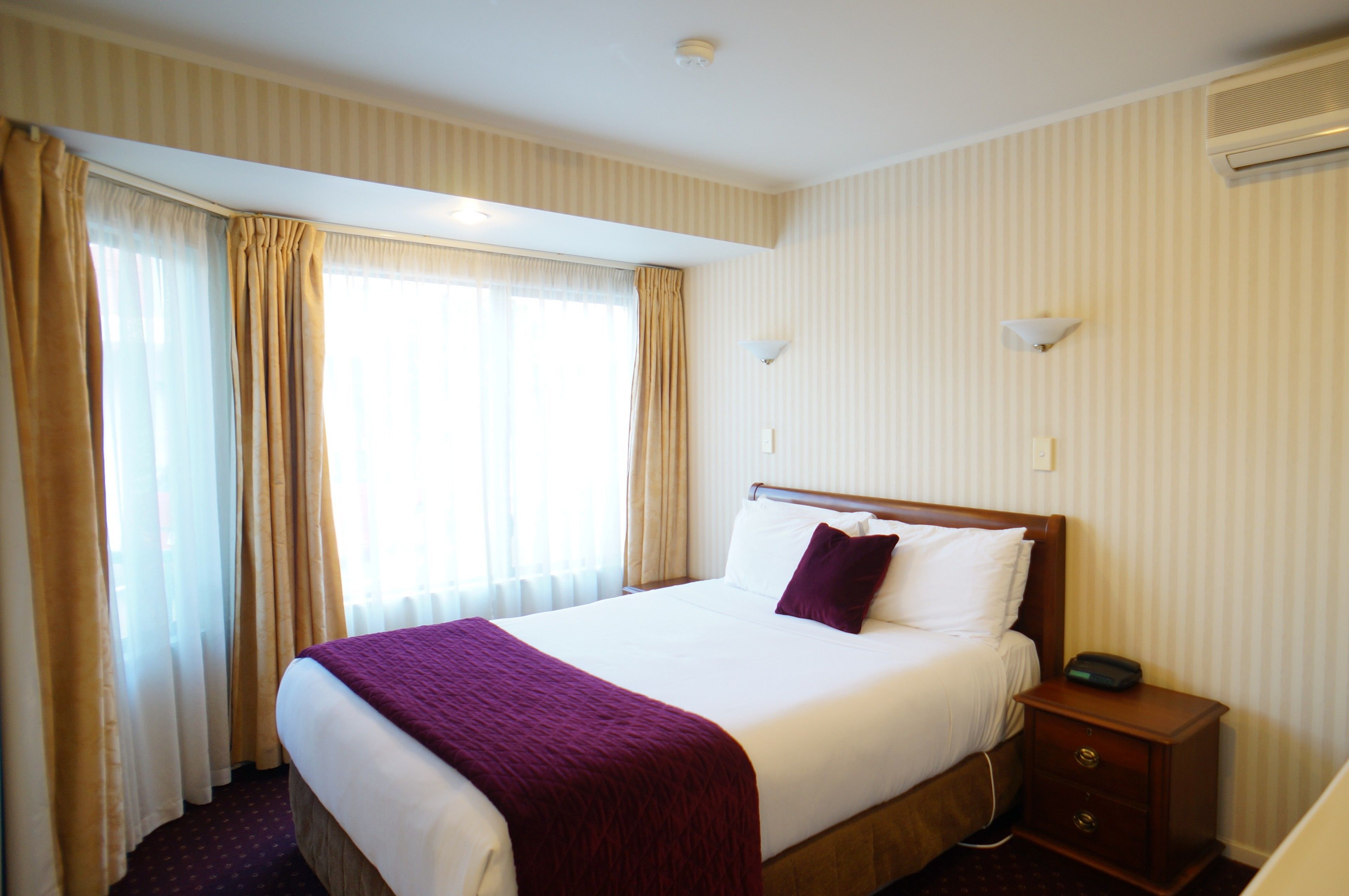 A hotel room with a large bed, a bedside table, a nightstand, and a window with curtains.