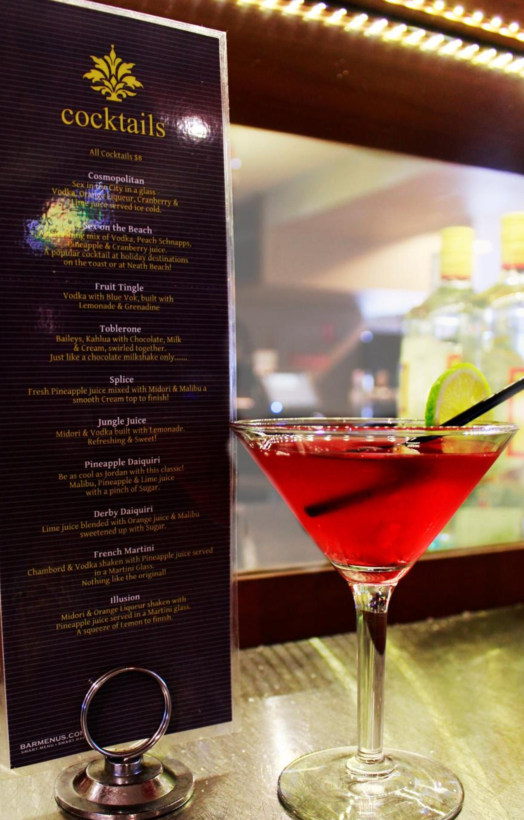 A cocktail menu with various drink options and a martini glass with a red cocktail.