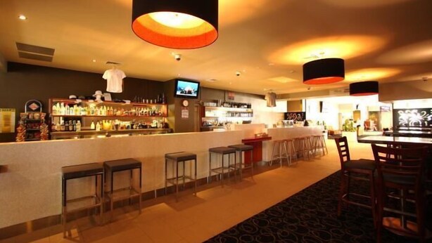 A bar area with a counter, stools, and a television screen. - Peden's Hotel (Cessnock)