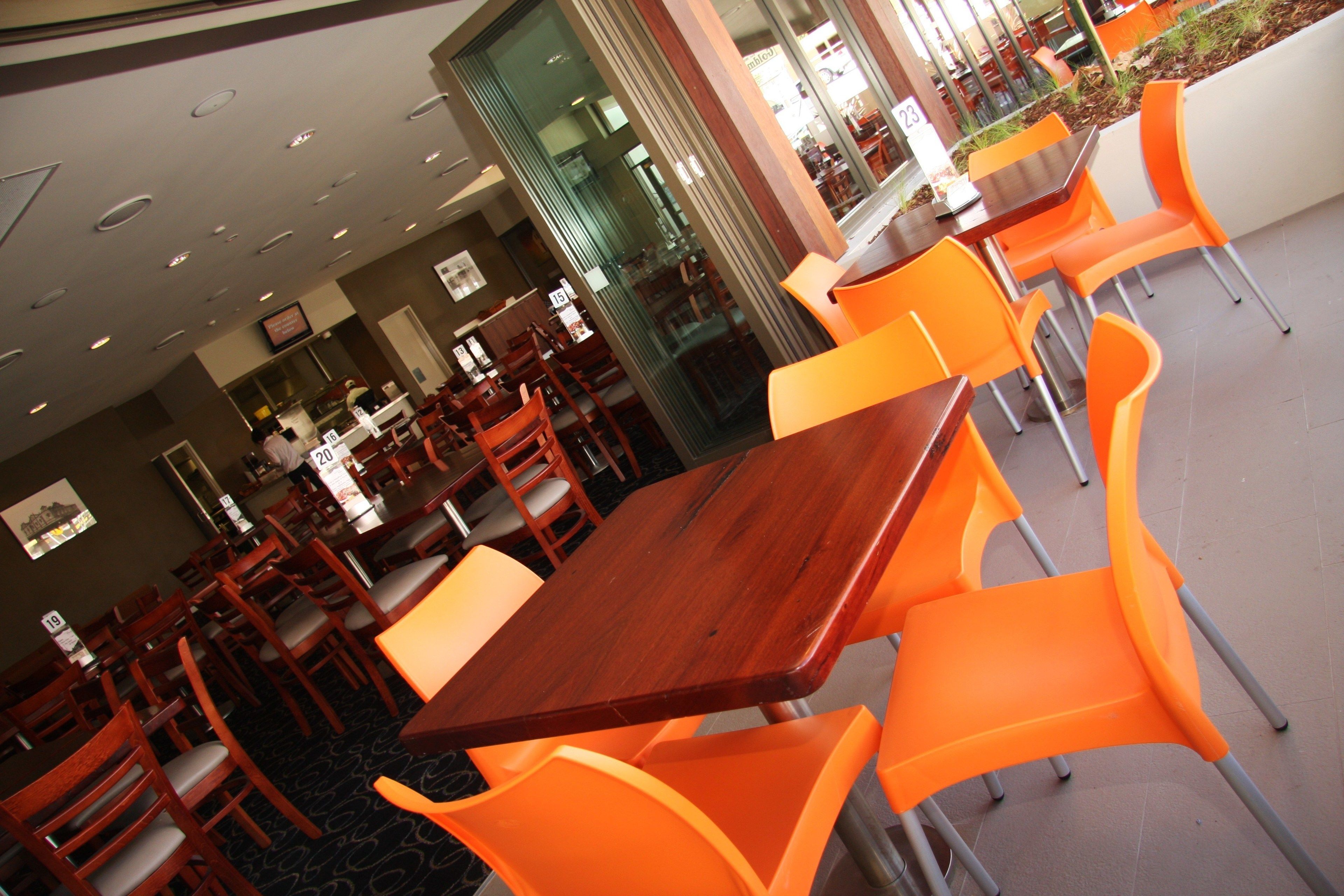 Een restaurant met houten tafels en oranje stoelen, een glazen scheiding en een betegelde vloer.