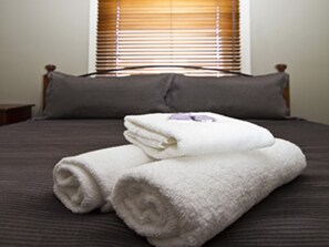 A neatly made bed with a dark bedspread, two pillows, and a stack of white towels. - Peden's Hotel (Cessnock)