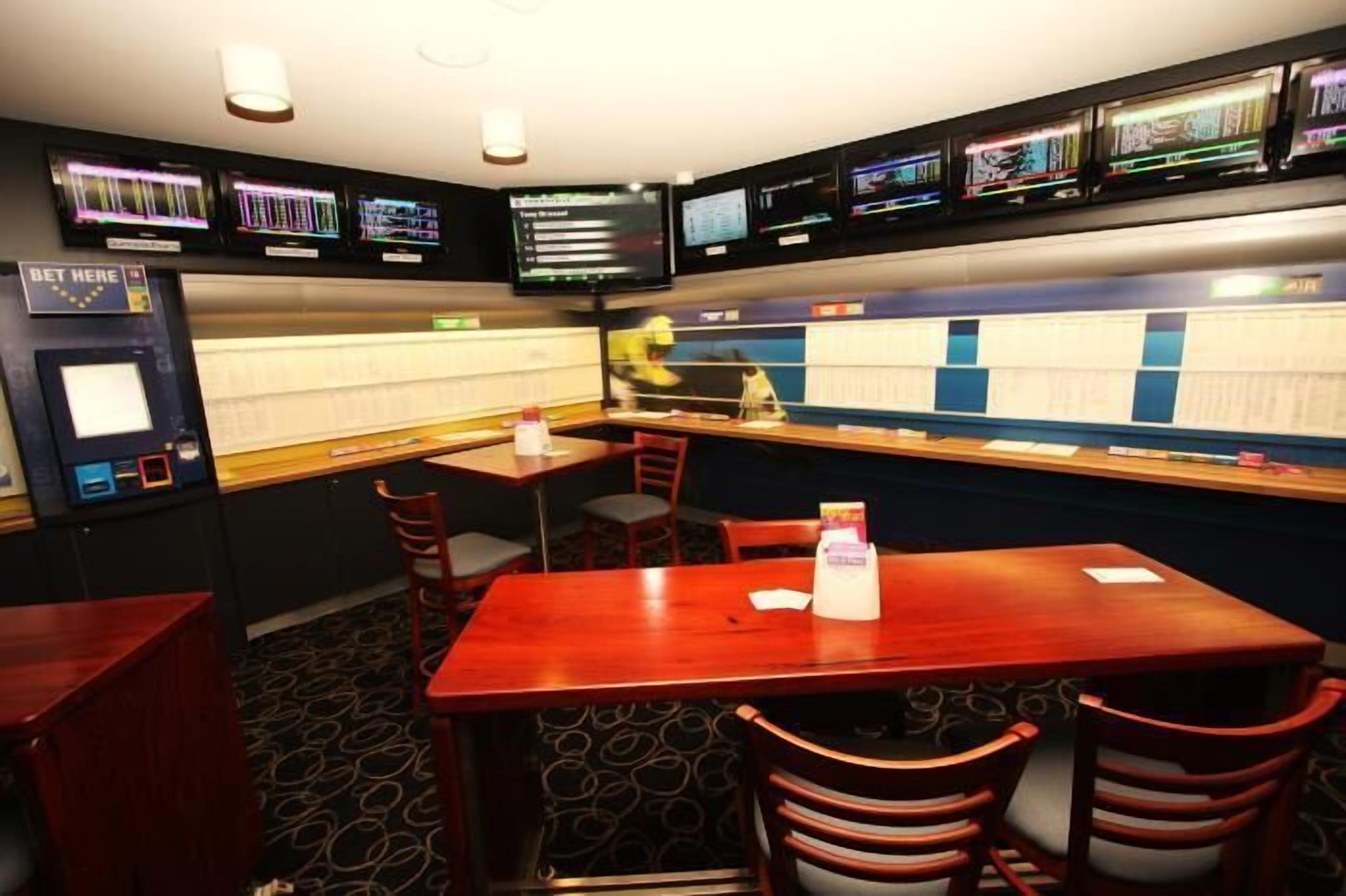 A room with multiple tables and chairs, a slot machine, and several screens displaying colorful graphics.